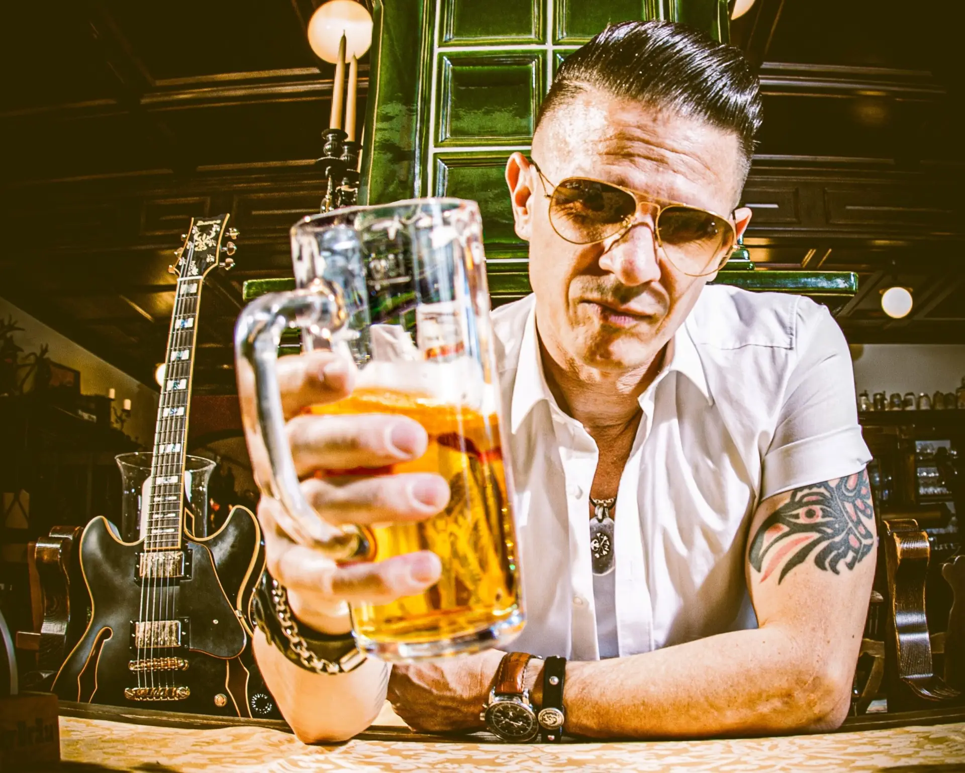 Der Musiker Fenzl sitzt mit einem Bier in der Hand an einem Tisch in der Sonne